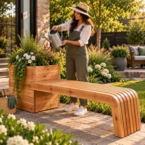 Puede incluir: Un banco de jardín de madera de cedro con una jardinera cuadrada integrada. El banco presenta un diseño de listones con un extremo curvo, mientras que la jardinera contiene follaje verde y flores blancas. Una cesta tejida con guantes verdes al lado.