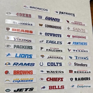 May include: A collection of rectangular stickers featuring the logos of various American football teams. The stickers display team names and logos in a variety of colors, including red, blue, and black. The teams include the Broncos, Patriots, 49ers, Giants, and others.