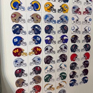 May include: A collection of rectangular stickers featuring various National Football League team helmet designs arranged in a grid. Each sticker displays a specific team logo and color scheme on a football helmet, including multiple professional franchises.
