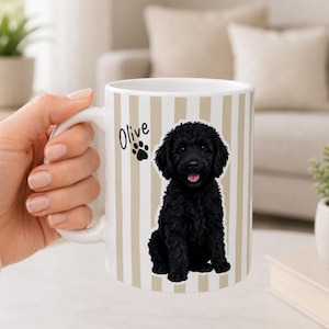 May include: White ceramic mug with vertical beige stripes, featuring a black dog illustration and the name "Olive" with a paw print. The mug has a white handle.