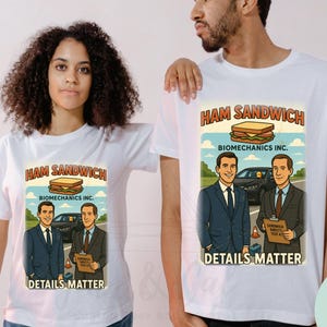 Puede incluir: Camisetas blancas con un gráfico retro que presenta un sándwich de jamón, el texto "HAM SANDWICH" y "DETAILS MATTER". El diseño incluye dos hombres con trajes y un coche. Las camisetas las llevan un hombre y una mujer.