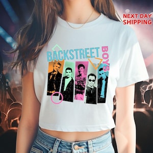 May include: White t-shirt featuring a graphic of the Backstreet Boys. The design includes the band's name in teal and pink, with images of the band members in colorful vertical panels. The shirt is a cropped style.