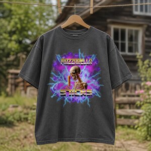 May include: A charcoal gray short-sleeve t-shirt featuring a graphic of a skeleton holding a mozzarella stick. The design includes purple clouds, blue lightning bolts, and the text MOZZARELLA STICKS in a metallic, block-style font.