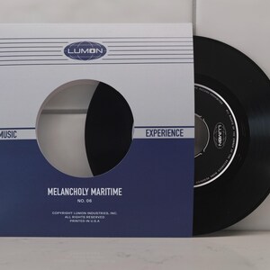 May include: A black vinyl record in a white and navy blue sleeve. The sleeve has the text "LUMON," "MUSIC," "EXPERIENCE," and "MELANCHOLY MARITIME." The record label is visible. The record is a classic music format.