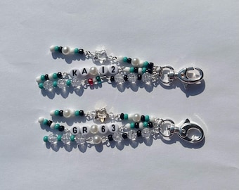 Peut inclure: Deux porte-clés perlés avec fermoirs argentés. Chaque porte-clés comporte des perles blanches, noires, turquoise et transparentes, avec les lettres "KA12" et "GR63" épelées en perles blanches. Des breloques en forme d'étoile et des perles de perles sont également incluses.