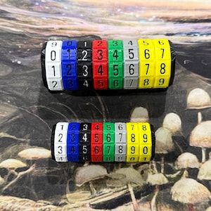 May include: Two colorful number wheels with black end caps. Each wheel has a series of numbers from 0 to 9 in various colors, including blue, red, green, and yellow. The wheels are likely used for puzzles or educational purposes.