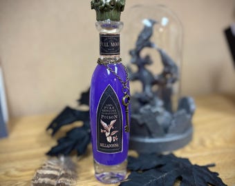 May include: A decorative glass bottle filled with purple liquid, labeled "Poison" with a key charm. The bottle has a detailed green stopper and is surrounded by black leaves and a feather. A glass dome with a statue is in the background.