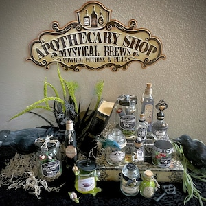 May include: A decorative sign reading APOTHECARY SHOP MYSTICAL BREWS POWDER POTIONS & PILLS above a collection of glass jars with labels like WITCH FINGERS, BONE POWDER, and TOADSTOOL, accompanied by two black crow figurines and green foliage.