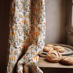 May include: A beige curtain with a repeating floral pattern in yellow, orange, and green hangs next to a wooden table. Several round loaves of bread sit on the table and a wooden tray.