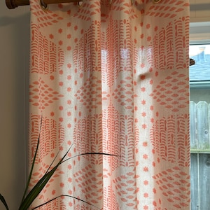 Pode incluir: Painéis de cortina creme com um padrão coral repetido de folhas estilizadas e estrelas. As cortinas são penduradas em uma haste de madeira com ilhós dourados. O design cria uma aparência macia e texturizada.