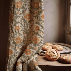 Peut inclure: Un rideau floral beige avec des motifs de fleurs orange et de feuilles vertes. Plusieurs miches de pain rondes sont posées sur une table en bois. Le rideau est drapé sur le côté, révélant le pain et un plateau en bois.