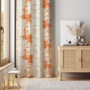 May include: Cream-coloured curtain with an abstract orange pattern. The design features large, irregular orange shapes against a grid of thin, reddish-brown lines. The curtain hangs in front of a window, adding a decorative element to the room.