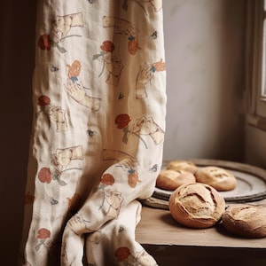 May include: Beige linen fabric with a repeating pattern of hands holding roses in shades of red and orange. Several round loaves of bread are on a wooden surface.