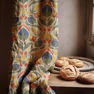 Puede incluir: Una cortina con estampado floral con flores y hojas azules, naranjas, amarillas y verdes. Varias hogazas de pan redondas están sobre una bandeja de madera, junto a la cortina.