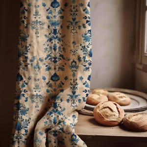 Può includere: Una tenda in tessuto beige con un motivo verticale ripetuto di fiori e damaschi blu. Il tessuto cade in morbide pieghe, mostrando una stampa botanica dettagliata in varie tonalità di blu su uno sfondo color marrone chiaro.