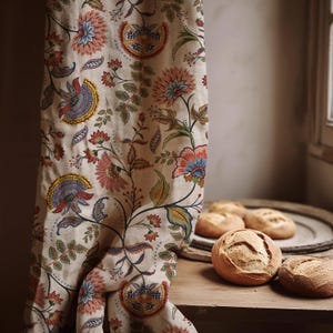 Puede incluir: Una cortina con estampado floral con fondo crema y flores coloridas en tonos rosa, azul y naranja. La cortina está sobre una superficie de madera con varias hogazas de pan redondas en una bandeja de madera.