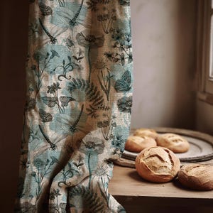 Può includere: Una tenda floreale con un motivo di libellule e farfalle nei toni del verde acqua, beige e grigio. La tenda è drappeggiata su una superficie di legno, con diverse pagnotte rotonde su un vassoio di legno.