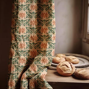 Puede incluir: Una tela beige con un estampado floral de hojas verdes y flores naranjas está drapeada sobre una superficie de madera. Varias hogazas de pan redondas se encuentran en una bandeja y mesa de madera, cerca de una ventana.