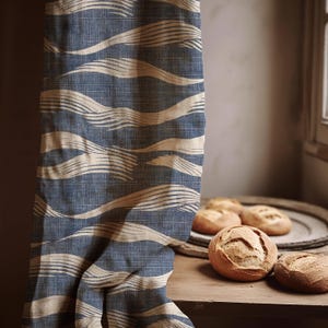 May include: Blue and beige patterned fabric curtain with a wave-like design. Several round loaves of bread are on a wooden table. A wooden tray holds additional bread. The curtain is hanging near a window.