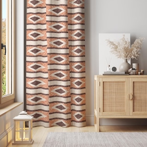 May include: A set of patterned curtains with a geometric design in shades of orange, brown, and cream. The curtains are hanging in front of a window, and the design features diamond and horizontal stripe patterns. The room also includes a wooden cabinet and decorative items.
