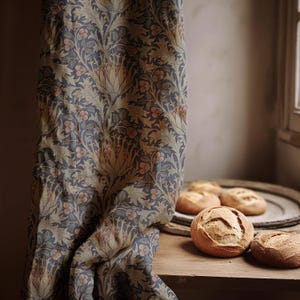 May include: A draped curtain with a floral pattern in shades of blue, green, and peach. The curtain is next to a wooden table with several round loaves of bread on a wooden tray.
