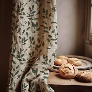 Könnte beinhalten: Ein beiger Leinenvorhang mit grünem Blättermuster hängt neben einem Holztisch. Auf dem Tisch und einem Holztablett liegen mehrere knusprige Brötchen. Der Vorhang hat ein sich wiederholendes dunkelgrünes Blattdesign.