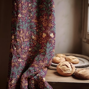 Könnte beinhalten: Ein Vorhang mit floralem Muster in Lila, Grün und Gold. Der Vorhang ist neben einer Holzoberfläche drapiert, auf der sich mehrere runde Brotlaibe befinden. Das Brot ist goldbraun.