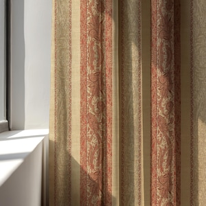 Peut inclure: Rideaux beiges et rouges à motifs cachemire. Les rideaux présentent des rayures verticales avec un fond beige et des motifs cachemire rouges. Ils sont suspendus devant une fenêtre, la lumière du soleil les traversant.