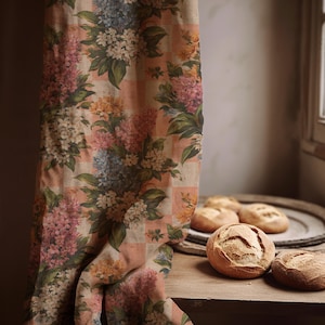 Op de afbeelding: Een bloemig gordijn met een perzik- en wit geruit patroon. Het gordijn toont clusters van roze, witte, blauwe en gele bloemen met groene bladeren. Verschillende ronde broden liggen op een houten oppervlak.