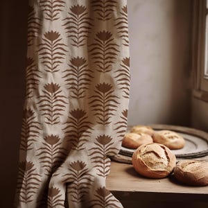 May include: A beige curtain with a repeating brown floral pattern hangs next to a wooden table. Several round loaves of bread sit on the table and a wooden tray. The curtain is draped over the table.