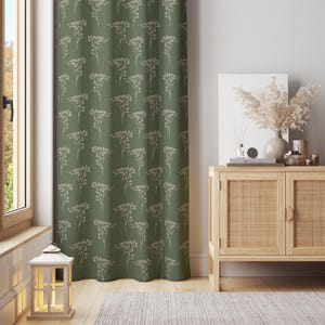 Puede incluir: Cortina verde con un patrón repetido de ramitas florales blancas. La cortina cuelga frente a una ventana. Un mueble de madera con frente tejido está a la derecha. Una linterna blanca está en el suelo.