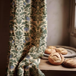 May include: A beige curtain with a repeating pattern of green leaves and blue flowers. The curtain is draped next to a wooden surface with several round loaves of bread on a wooden tray.