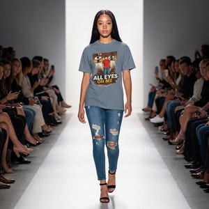 May include: A model walks a runway wearing a blue t-shirt with the text "ALL EYES ON ME" and a graphic of a person. The model is also wearing blue jeans with distressed patches and black heels.