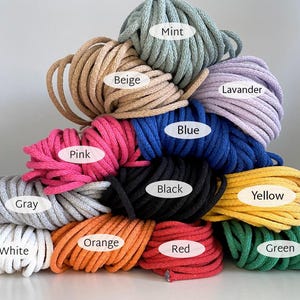 May include: A selection of macrame cords in a range of colours: mint, beige, pink, blue, black, yellow, orange, red, and green. Each cord is labelled with its colour name. Ideal for crafting and DIY projects.