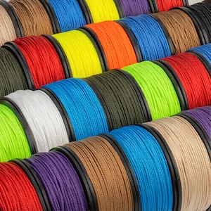 May include: A close-up shot of multiple spools of colorful thread. The thread is tightly wound on black spools, with colors including red, yellow, blue, green, and brown. The threads appear to be made of a durable material.