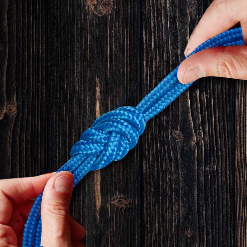 Pu&ograve; includere: Primo piano di una corda blu annodata. La corda &egrave; tenuta da due mani su uno sfondo di legno scuro. Il nodo &egrave; ben intrecciato, mostrando la consistenza e il colore della corda. L'immagine mette in evidenza l'artigianato del nodo.