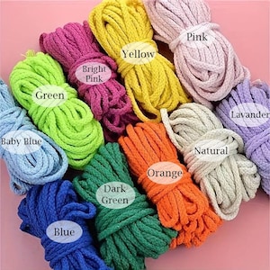 May include: A collection of colorful macrame cords in various shades, including baby blue, green, yellow, pink, and orange. Each bundle is labeled with its color name. The cords are tightly wound and ready for crafting projects.