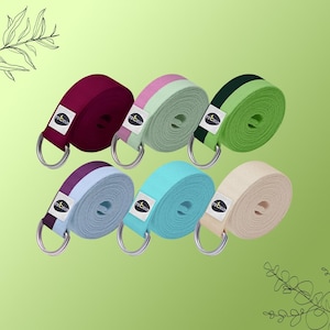 Puede incluir: Un conjunto de correas de yoga en varios colores, incluyendo burdeos, verde y azul. Cada correa está enrollada y presenta un anillo en D de metal y una pequeña etiqueta blanca con texto negro. Estas correas están diseñadas para yoga y ejercicios de estiramiento.