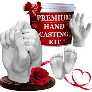 May include: A hand casting kit with a red bow, a red rose, and a heart-shaped ribbon. The kit includes a cast of two hands holding each other, a baby's hand, and baby feet. The kit's container is red with white text that reads "PREMIUM HAND CASTING KIT."