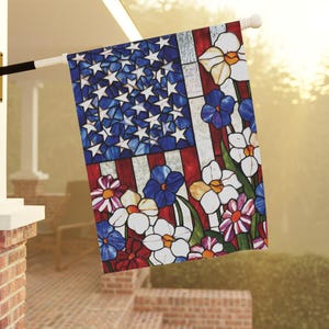 May include: A decorative garden flag featuring a stained-glass design of the American flag with white stars on a blue background and red and white stripes. The flag is adorned with colorful flowers.