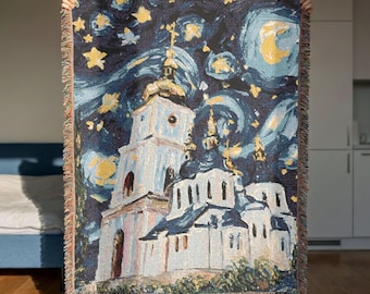 May include: A woven throw blanket featuring a dark blue night sky with yellow stars and a crescent moon above a white church building with gold domes. The blanket has a fringed edge and a textured, tapestry-style appearance.