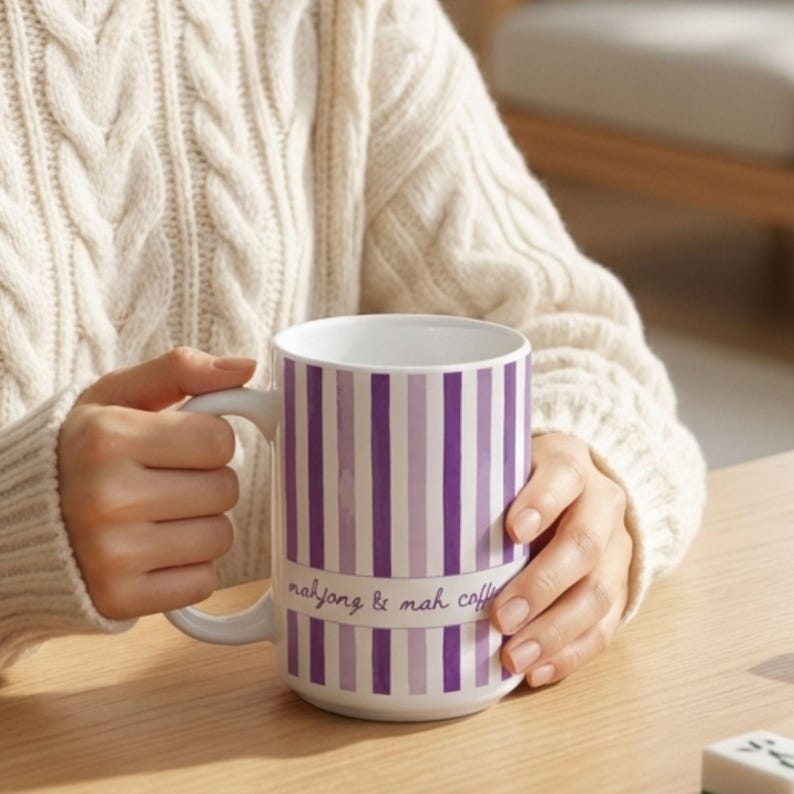 Puede incluir: Una taza de cer&aacute;mica blanca con rayas verticales en tonos alternos de morado y lavanda. La taza tiene un asa curva y muestra el texto mahjong & mah coffee en una fuente cursiva de color morado en el centro del patr&oacute;n de rayas.