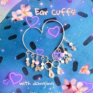 May include: Silver-toned ear cuff in a heart shape, adorned with freshwater pearls, dangling Swarovski crystals, and leaf charms. The text reads "Freshwater Pearl Ear Cuffs!" and "with dangling swarovski crystals."