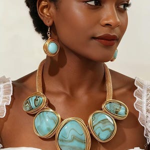 May include: A gold-toned statement necklace and matching drop earrings featuring large, smooth, light blue and brown marbled stones encased in intricate gold wire wrapping. The necklace consists of five prominent oval-shaped stones.