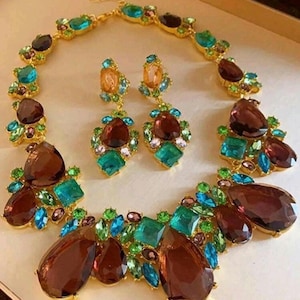 May include: A gold-tone necklace and matching earring set featuring large teardrop-shaped brown crystals accented with smaller bright turquoise, emerald green, and light pink faceted stones arranged in a cluster design with a metal chain.