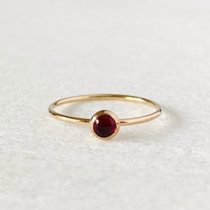 May include: A simple gold band ring with a single round red gemstone.