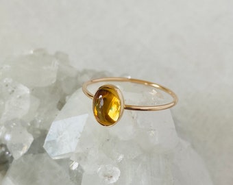 May include: A gold ring with a yellow oval gemstone set in the center. The ring is resting on a bed of white crystals.