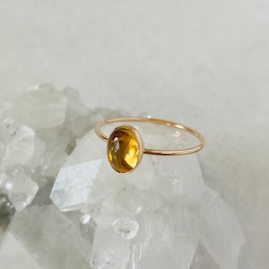 Peut inclure: Une bague en or avec une pierre précieuse ovale jaune sertie au centre. La bague repose sur un lit de cristaux blancs.