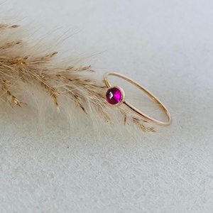 May include: A delicate gold ring with a single, round, bright pink gemstone.
