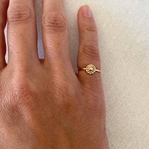May include: A gold ring with a small, round, textured design in the center.